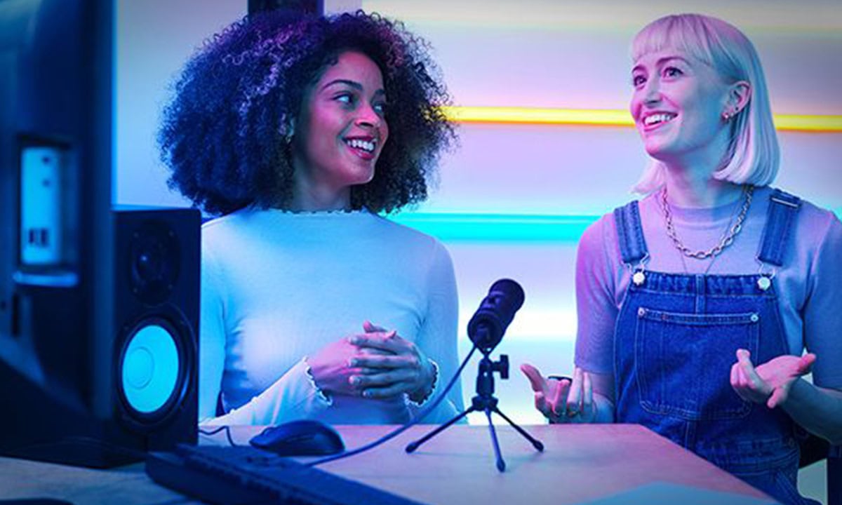 Twee vrouwen in een creatieve studio met professionele audio- en videoapparatuur, waaronder een microfoon en speakers, voor gaming en contentcreatie.